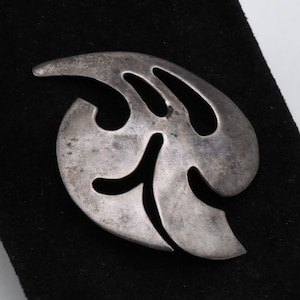 Op de afbeelding: Een zilverkleurige abstracte broche in de vorm van een blad met uitgesneden details.