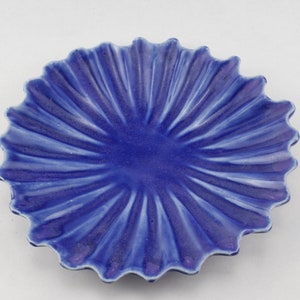May include: A blue ceramic dish with a scalloped edge and a sunburst design. The dish is made of glazed ceramic and has a smooth, shiny finish.
