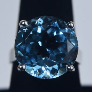 K&ouml;nnte beinhalten: Ein runder blauer Topas-Edelsteinring, der in eine silberne Fassung gefasst ist. Der Ring hat vier Krappen, die den Stein an Ort und Stelle halten.