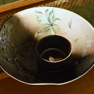 May include: A white ceramic serving bowl with a black glaze and a floral design. The bowl has a smaller, black bowl inside.