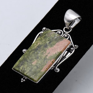 May include: A silver pendant with a green and pink stone set in a decorative frame.