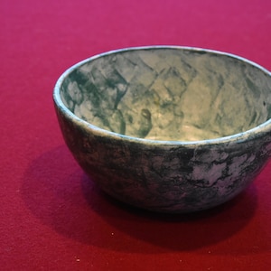 Puede incluir: Un cuenco de cerámica verde y blanco con un diseño de mármol. El cuenco está vacío y está sobre una superficie roja.