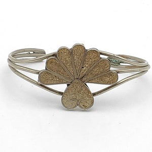 Puede incluir: Una pulsera de plata con un diseño en forma de abanico de color dorado. La pulsera está hecha de tres bandas finas de metal.