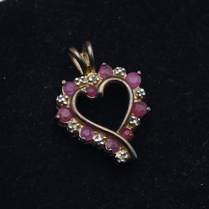 May include: A silver heart-shaped pendant with a pink gemstone border. The pendant is set with small, clear gemstones.