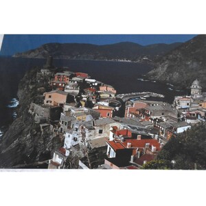 May include: An aerial view of a colourful village built on a cliff overlooking a blue ocean. The village is made up of many small, brightly coloured buildings with red tile roofs. The ocean is calm and blue, and the sky is a clear blue.