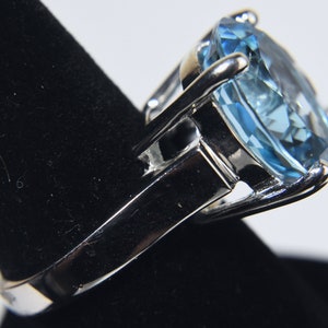 K&ouml;nnte beinhalten: Ein silberner Ring mit einem gro&szlig;en, hellblauen Edelstein. Der Edelstein ist im Kissen-Schliff geschliffen und hat eine facettierte Oberfl&auml;che.