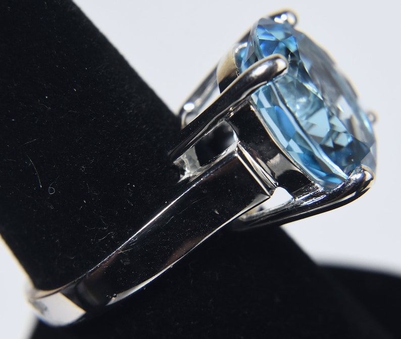 K&ouml;nnte beinhalten: Ein silberner Ring mit einem gro&szlig;en, hellblauen Edelstein. Der Edelstein ist im Kissen-Schliff geschliffen und hat eine facettierte Oberfl&auml;che.