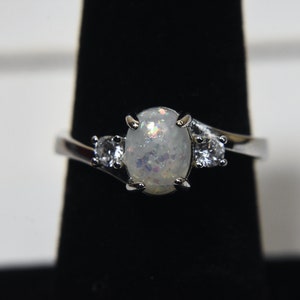 May include: A silver ring with a large oval white opal gemstone and two smaller clear round gemstones.