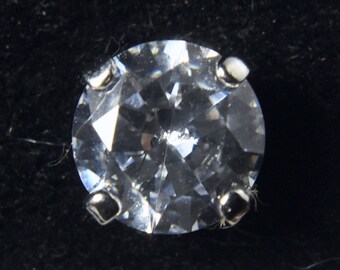 May include: A clear round gemstone with a silver setting. The gemstone is set in a prong setting with four prongs.
