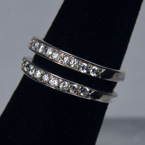 May include: Two silver rings with a row of clear cubic zirconia stones on each band.