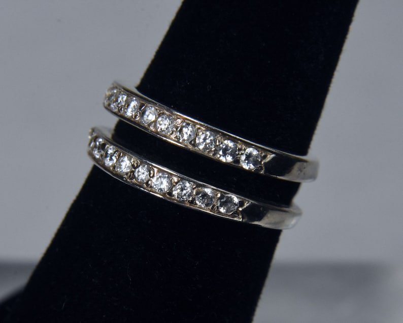May include: Two silver rings with a row of clear cubic zirconia stones on each band.