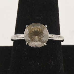 May include: A silver ring with a large, clear, faceted gemstone. The gemstone has a light brown hue and a unique, star-shaped pattern.