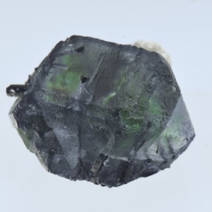 May include: A dark green and gray fluorite crystal with a sharp, faceted shape. The crystal has a translucent appearance and shows some internal striations.