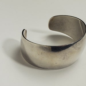 May include: A silver bangle bracelet with a smooth, rounded surface.