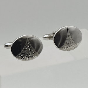 May include: A pair of silver cufflinks with a geometric design. The cufflinks are oval shaped and have a silver finish.