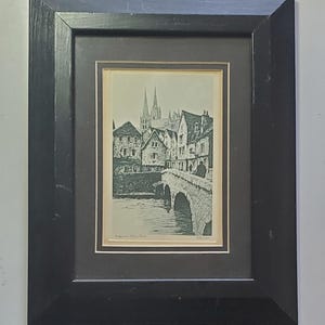 May include: A black and white print of a bridge over a river in a European town. The print is framed in a black frame with a gold mat. The text "Bridge over a Loire River" is visible at the bottom of the print.