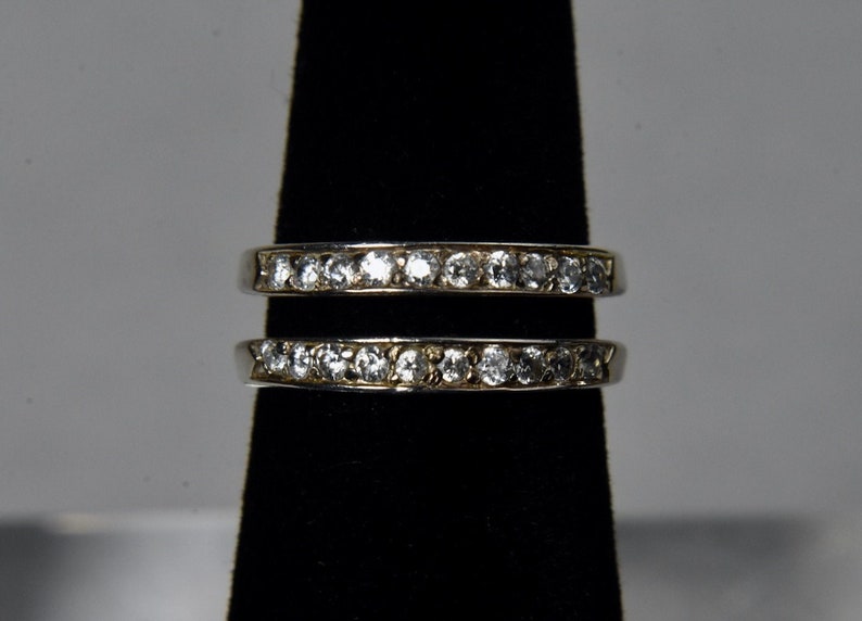 May include: Two silver rings with a row of clear cubic zirconia stones on each band.