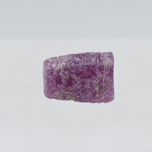 May include: A rough, pink, and purple gemstone with a slightly rectangular shape.
