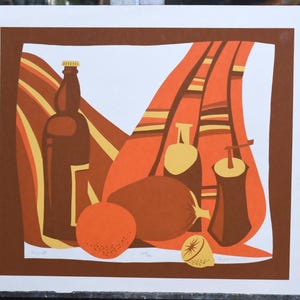 Könnte beinhalten: Ein Stillleben-Druck mit einer braunen Glasflasche, zwei orangenen Früchten, einer braunen Flasche und einem braunen und orangefarbenen gestreiften Tuch. Der Druck ist auf weißem Hintergrund mit braunem Rand.