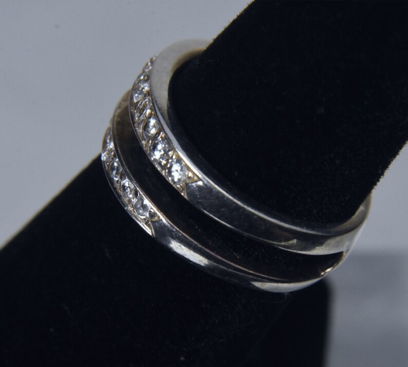 May include: Two silver rings with a row of small clear stones set into the band.