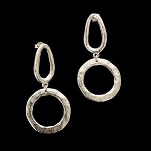 Könnte beinhalten: Ein Paar silberfarbene Ohrhänger mit gehämmertem Finish. Jeder Ohrring besteht aus einem länglichen, unregelmäßigen ovalen Glied an der Oberseite, das mit einem kreisförmigen Ring an der Unterseite verbunden ist, was ein hängendes Design ergibt.