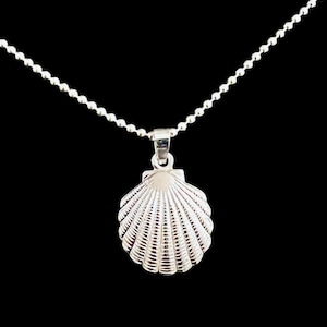Könnte beinhalten: Halskette mit silbernem Muschel-Anhänger. Der Anhänger ist ein detailliertes, dreidimensionales Muscheldesign. Die Halskette ist eine feine Kugelkette. Der Hintergrund ist einfarbig schwarz.