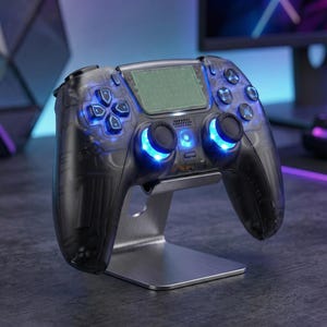 May include: A transparent black games controller with blue LED lights, on a silver stand. The controller has a central screen and multiple buttons. The design is modern and sleek, suitable for video game enthusiasts.