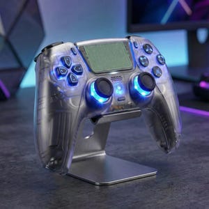 May include: A clear gaming controller with blue LED illumination, presented on a silver stand. The controller has a D-pad, action buttons, and analogue sticks. The design is modern and sleek, suitable for video game enthusiasts.