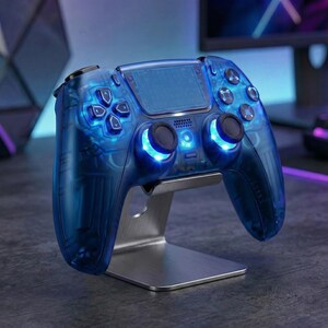 May include: A transparent blue gaming controller with illuminated buttons and joysticks, resting on a silver metal stand. The controller features a D-pad, face buttons, and shoulder buttons. The overall design is sleek and modern, with a focus on aesthetics.