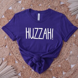 May include: A purple t-shirt with the word "HUZZAH!" printed in white on the front.