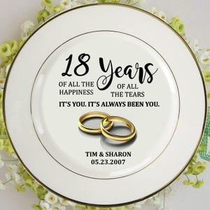 May include: A white decorative plate with a gold rim and the text "18 Years" in black script. The plate features two gold wedding rings and the inscription "Of all the happiness, of all the tears. It's you. It's always been you." The names "Tim & Sharon" and the date "05.23.2007" are also included.