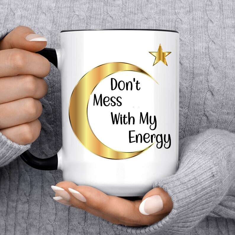 Puede incluir: Taza de cer&aacute;mica blanca con interior y asa negros. La taza presenta un dise&ntilde;o de media luna y estrella doradas con el texto "Don't Mess With My Energy" en negro. Un regalo elegante y motivador.