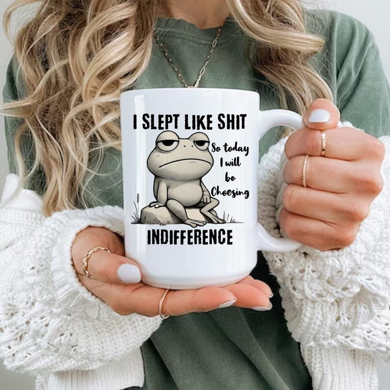 May include: White ceramic mug with a black and white illustration of a frog sitting on a rock. The mug has the text "I slept like shit so today I will be choosing indifference" printed on it.