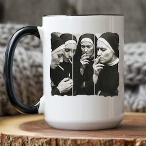 May include: White ceramic coffee mug with a black handle and rim. The mug features a black and white image of four nuns smoking cigarettes. The image is a collage of four separate panels.