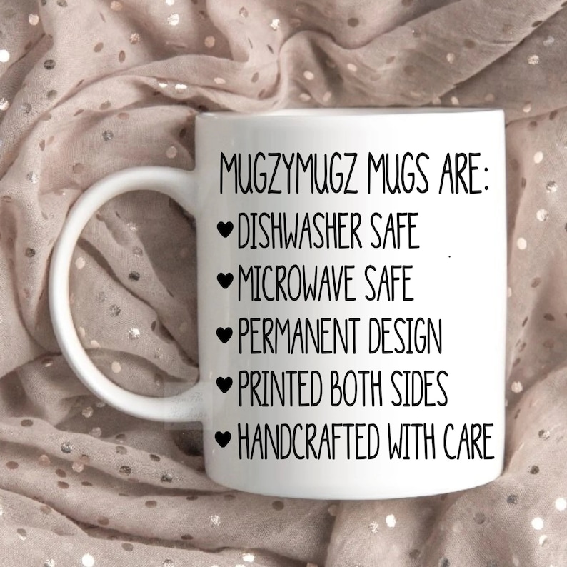 May include: White ceramic mug with black text that reads "MUGZYMUGZ MUGS ARE:  ❤DISHWASHER SAFE ❤MICROWAVE SAFE ❤PERMANENT DESIGN ❤PRINTED BOTH SIDES ❤HANDCRAFTED WITH CARE"