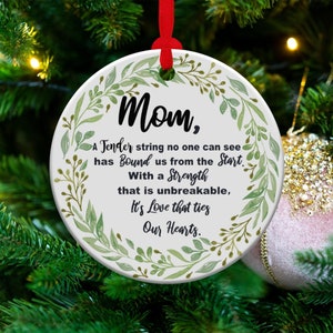 May include: White round ornament with a green leafy border and the text "Mom, A Tender string no one can see has Bound us from the Start. With a Strength that is unbreakable, It's Love that ties Our Hearts."