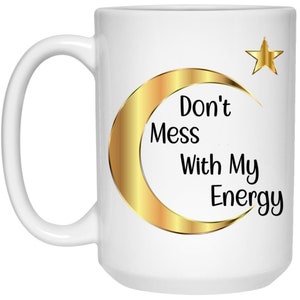 Puede incluir: Taza de cer&aacute;mica blanca con un dise&ntilde;o de luna creciente y estrella doradas. La taza presenta el texto "Don't Mess With My Energy" en negro. Tiene un asa grande y es adecuada para bebidas fr&iacute;as o calientes.