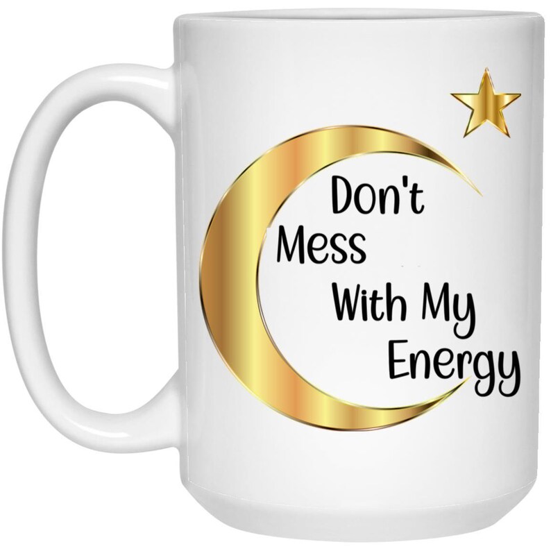Puede incluir: Taza de cer&aacute;mica blanca con un dise&ntilde;o de luna creciente y estrella doradas. La taza presenta el texto "Don't Mess With My Energy" en negro. Tiene un asa grande y es adecuada para bebidas fr&iacute;as o calientes.