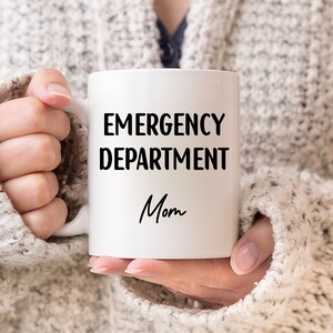 Pu&ograve; includere: Tazza in ceramica bianca con le parole "EMERGENCY DEPARTMENT Mom" in lettere nere. La tazza &egrave; tenuta da una persona che indossa un maglione grigio chiaro.