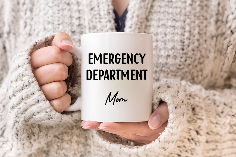 Pu&ograve; includere: Tazza in ceramica bianca con le parole "EMERGENCY DEPARTMENT Mom" in lettere nere. La tazza &egrave; tenuta da una persona che indossa un maglione grigio chiaro.