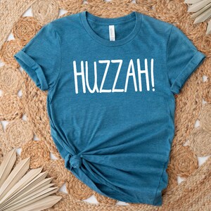 May include: A teal blue t-shirt with the word "HUZZAH!" printed in white on the front.