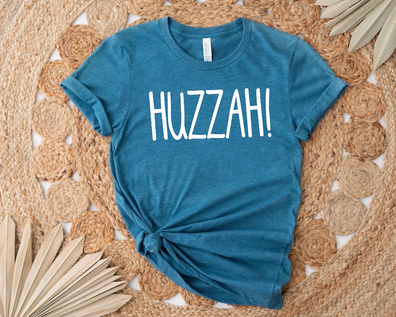 May include: A teal blue t-shirt with the word "HUZZAH!" printed in white on the front.
