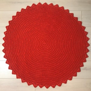 May include: A round, red crocheted rug with a scalloped edge. The rug is made of a thick, textured yarn and has a circular pattern.