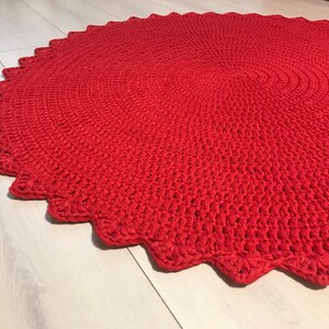 May include: A red crocheted round rug with a scalloped edge.