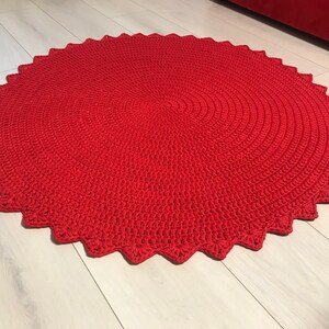 May include: A red crocheted round rug with a scalloped edge. The rug is made with a thick yarn and has a textured surface.