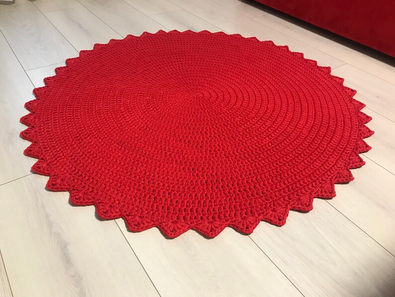 May include: A red crocheted round rug with a scalloped edge. The rug is made with a thick yarn and has a textured surface.