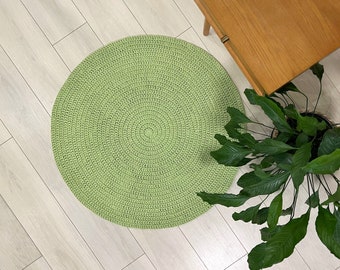 May include: A round, green crocheted rug with a textured surface. The rug is on a light wood floor.