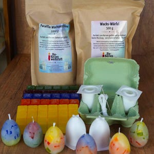 Könnte beinhalten: Ein Set zum Kerzenziehen und Kerzen gießen mit Wachspastillen, Wachswürfeln, eiförmigen Kerzenformen, Dochten und einem Eierkarton aus Pappe. Die Verpackung zeigt den Text "Paraffin Wachspastillen 1000 g" und "Wachs-Würfel 500 g".