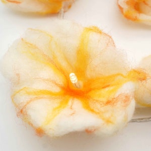 Könnte beinhalten: Eine weiße Filzblume mit orangefarbenen und gelben Akzenten, beleuchtet von einem kleinen LED-Licht in der Mitte.