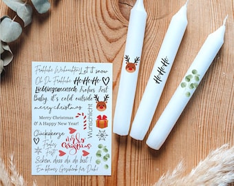 Op de afbeelding: Drie witte kaarsen met feestelijke kerst stickers. De stickers bevatten een rendier, sneeuwvlokken, een cadeaudoos, een snoepstok en de tekst "HoHoHo", "Merry Christmas", "Wunschlicht", "Glückskerze", "Frohes Fest", "Schön, dass du da bist!" en "Ein kleines Geschenk für Dich!"